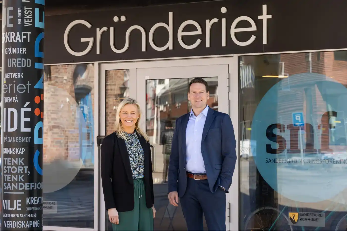 Bilde av daglig leder ved Gründeriet Benedicte sammen med forretningsutvikler ved Gründeriet Lars. De står sammen, utenfor dørene til Gründeriet sine lokaler i Sandefjord.