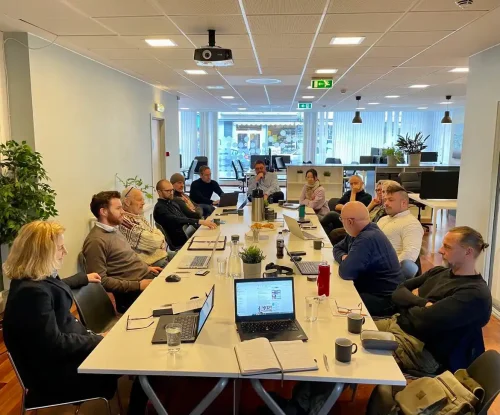 Bilde av et fellesmøte på Gründeriet. Bilde viser mennesker rundt et møtebord. I lyse og trivelige lokaler.